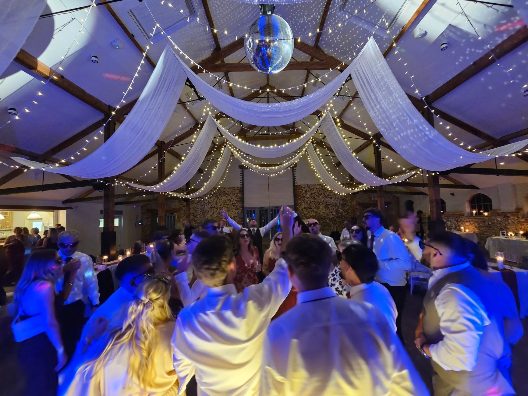 Wedding guests dancing under draped fairy lights and a mirror ball
