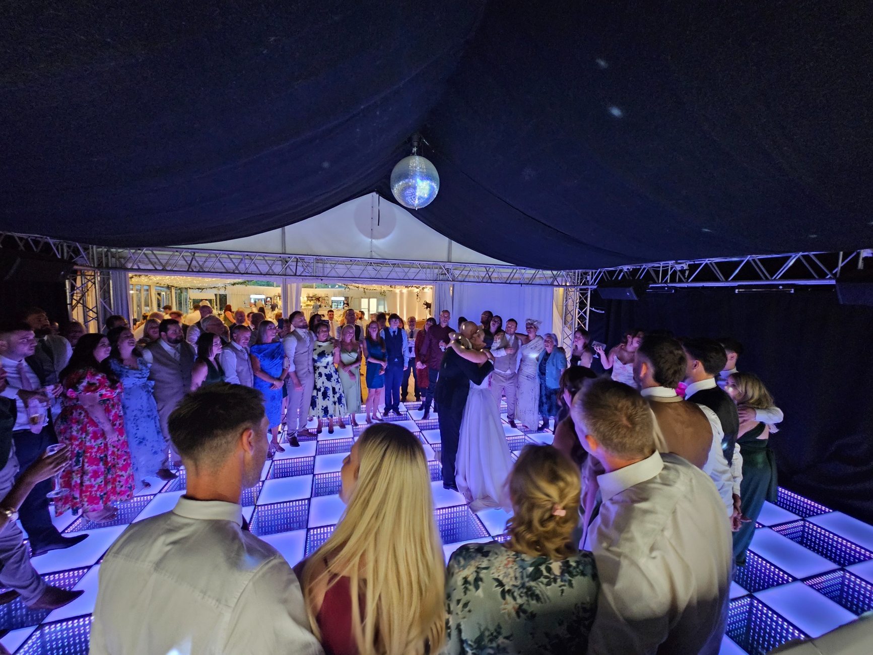 Wedding guests gathered around a couple on an illuminated dance floor